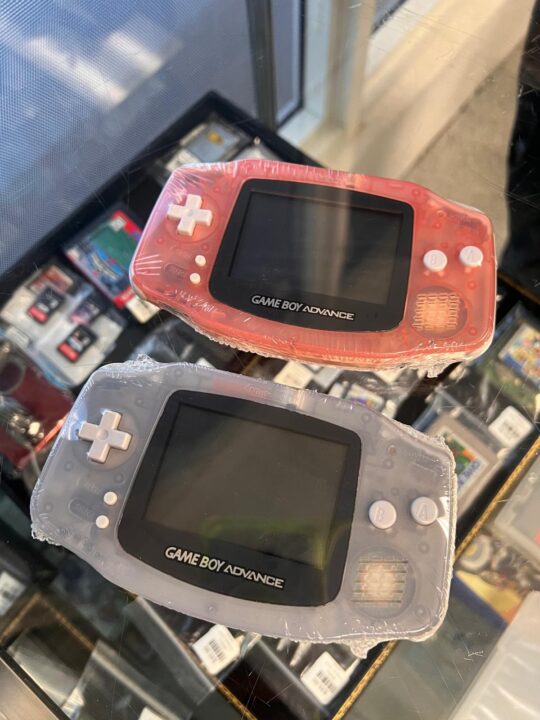 Two Nintendo Game Boy Advance handheld consoles, one pink and one clear, available at Dixie Pawn in Hollywood, FL.