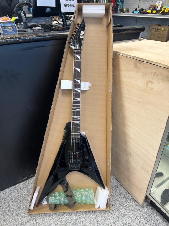 A sleek black electric guitar in its packaging, available at Dixie Pawn in Hollywood, Florida.