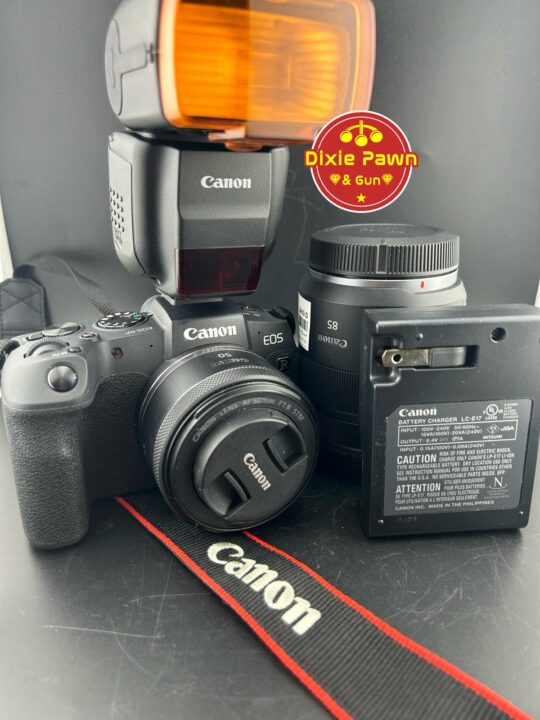 A Canon EOS RP mirrorless camera with an attached flash, extra lens, battery charger, and branded strap, showcased for sale at Dixie Pawn in Hollywood, Florida.